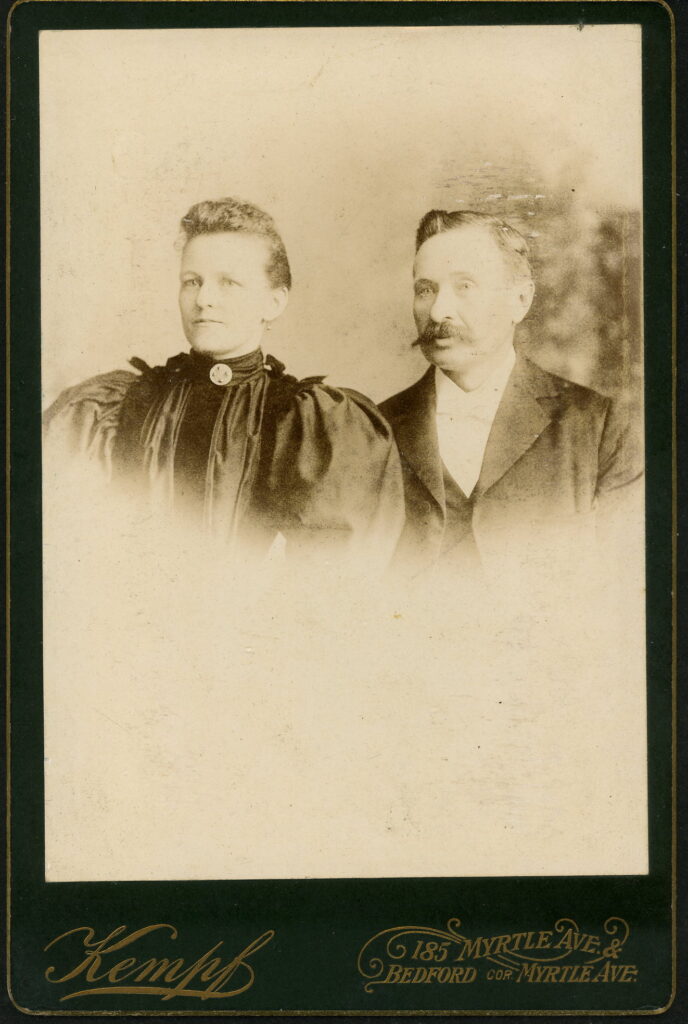 A monochrome photographic portrait from between 1865 and the 1920s taken in Kempf's Art Studios, 185 Myrtle Avenue, Brooklyn, NY